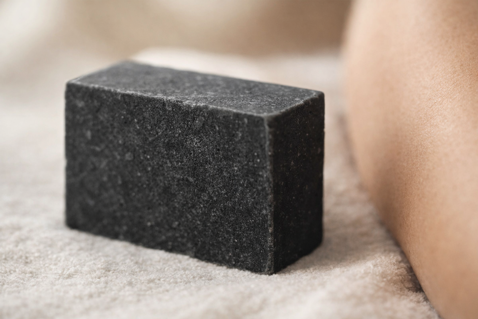 Black charcoal soap bar with textured surface placed on a soft neutral background, highlighting its deep cleansing appearance and minimalist skincare aesthetic