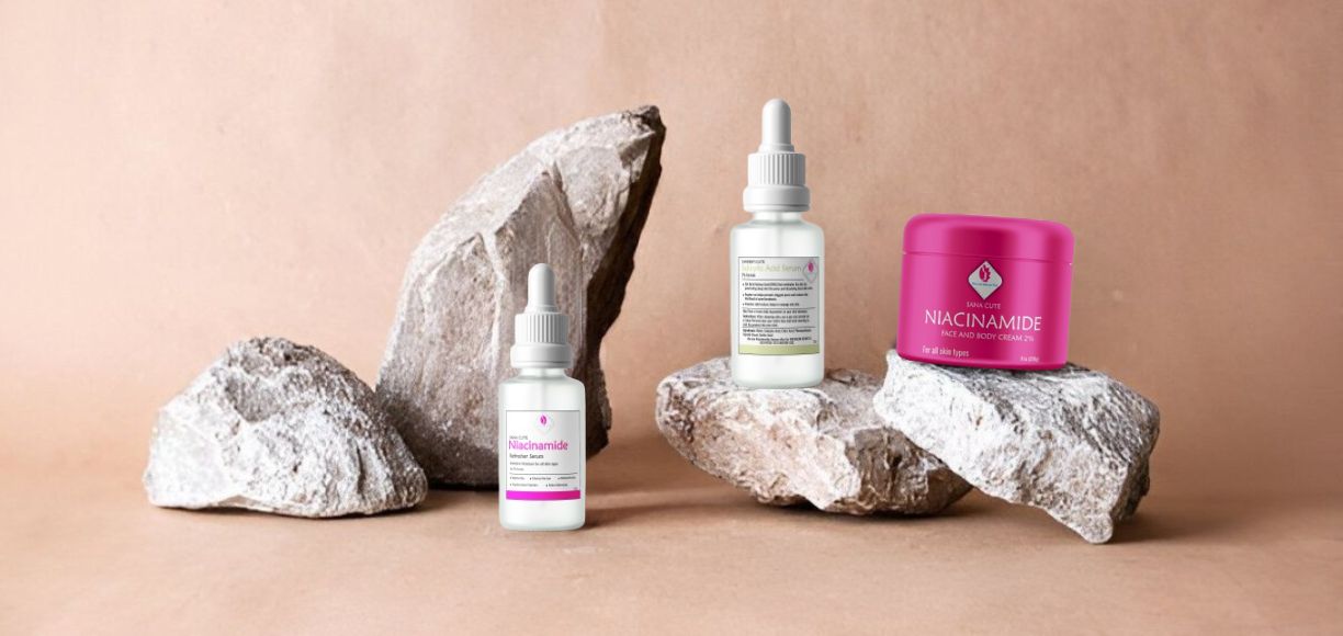 Pink Lady Bath and Body Niacinamide face and body cream in a bright pink jar and two serum dropper bottles, elegantly displayed on natural stones against a warm, earthy background.